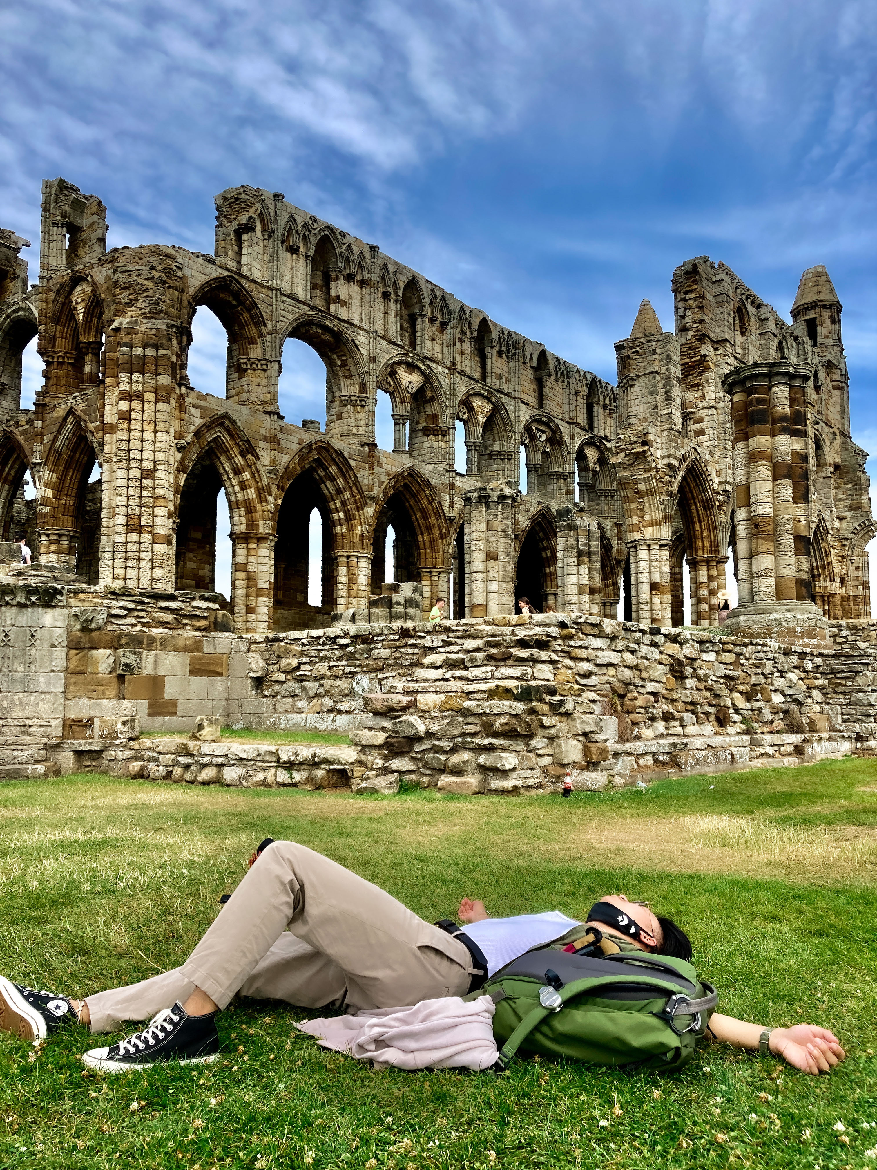 A photo of a student lying on the grass with the Whitby Abbey's gothic ruins in the backdrop.