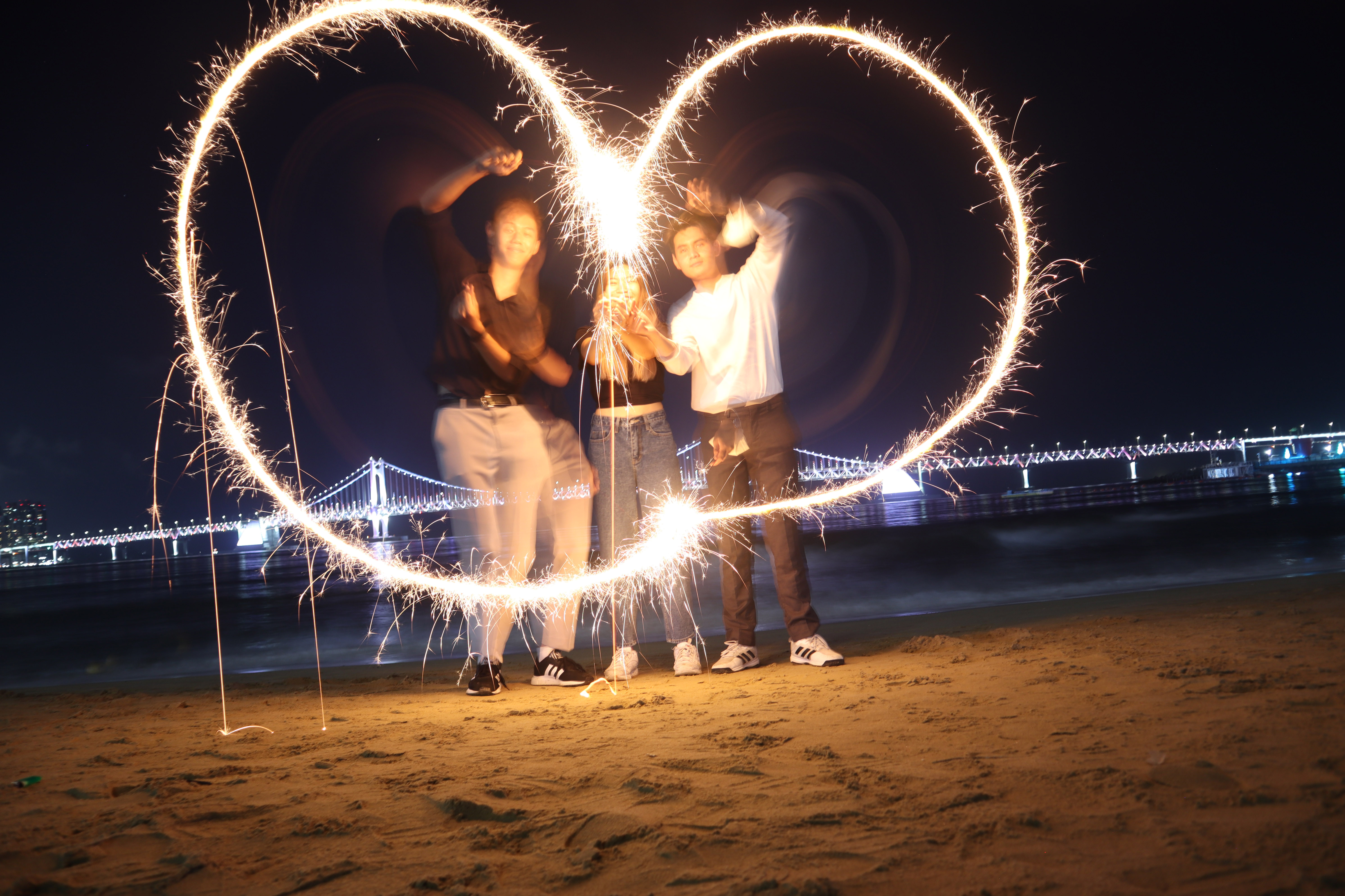 Photo of three students, at night, attempting to make a heart shape with fireworks.