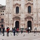 Photo of a plaza in Italy. There are people walking around taking pictures. Old buildings surround the plaza.