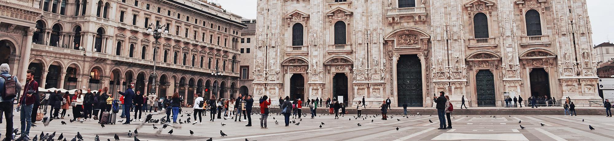 Photo of a plaza in Italy. There are people walking around taking pictures. Old buildings surround the plaza.