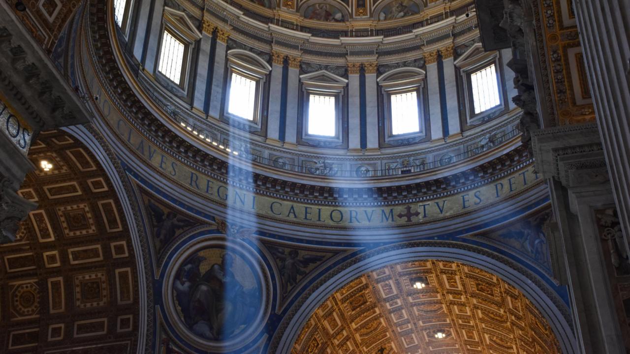 Photo of the inside of Saint Peter’s Basilica, showing beams of light glistening through the windows.