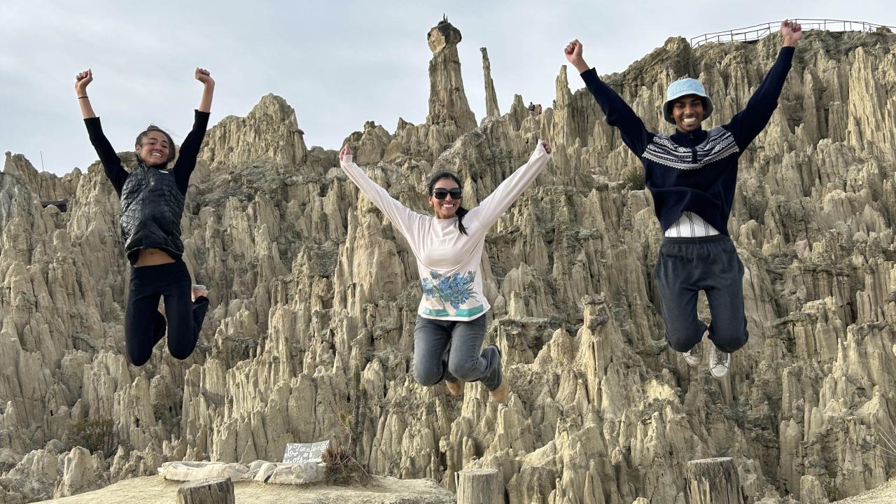 Three individuals joyfully jump in the air with rocky formations in the background.