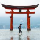 A man stands in calm water, reflecting the serene surroundings and the clear sky above.