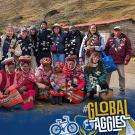 A group of UC Davis students and local community members in traditional clothing pose together outdoors in a mountainous rural area. Some people are wearing garlands made of white flowers. The women in the front row are dressed in vibrant woven garments, with colorful skirts and headwear. The students stand behind them, smiling, many dressed in casual outdoor gear. In the bottom left corner, the UC Davis Global Affairs logo is visible, and in the bottom right, the hashtag '#GlobalAggies' is displayed.