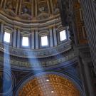 Photo of the inside of Saint Peter’s Basilica, showing beams of light glistening through the windows.
