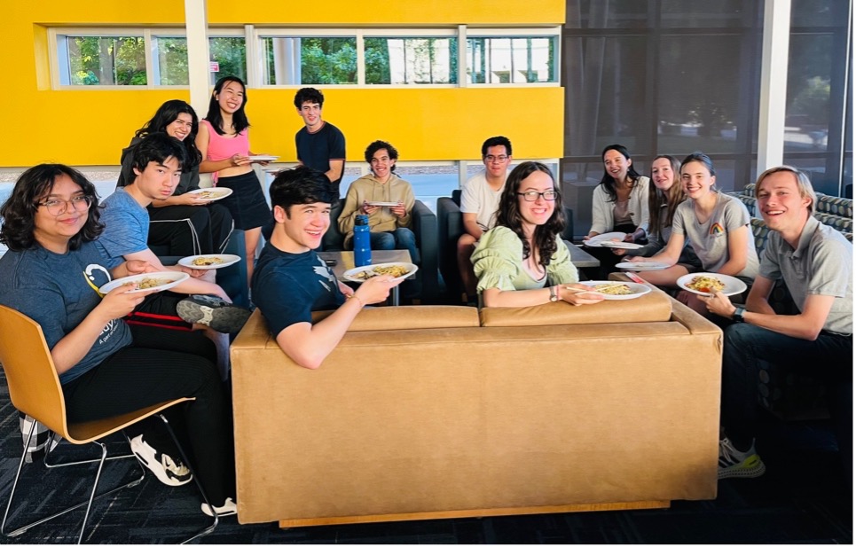 Group of students sit around a table and smile for the camera.