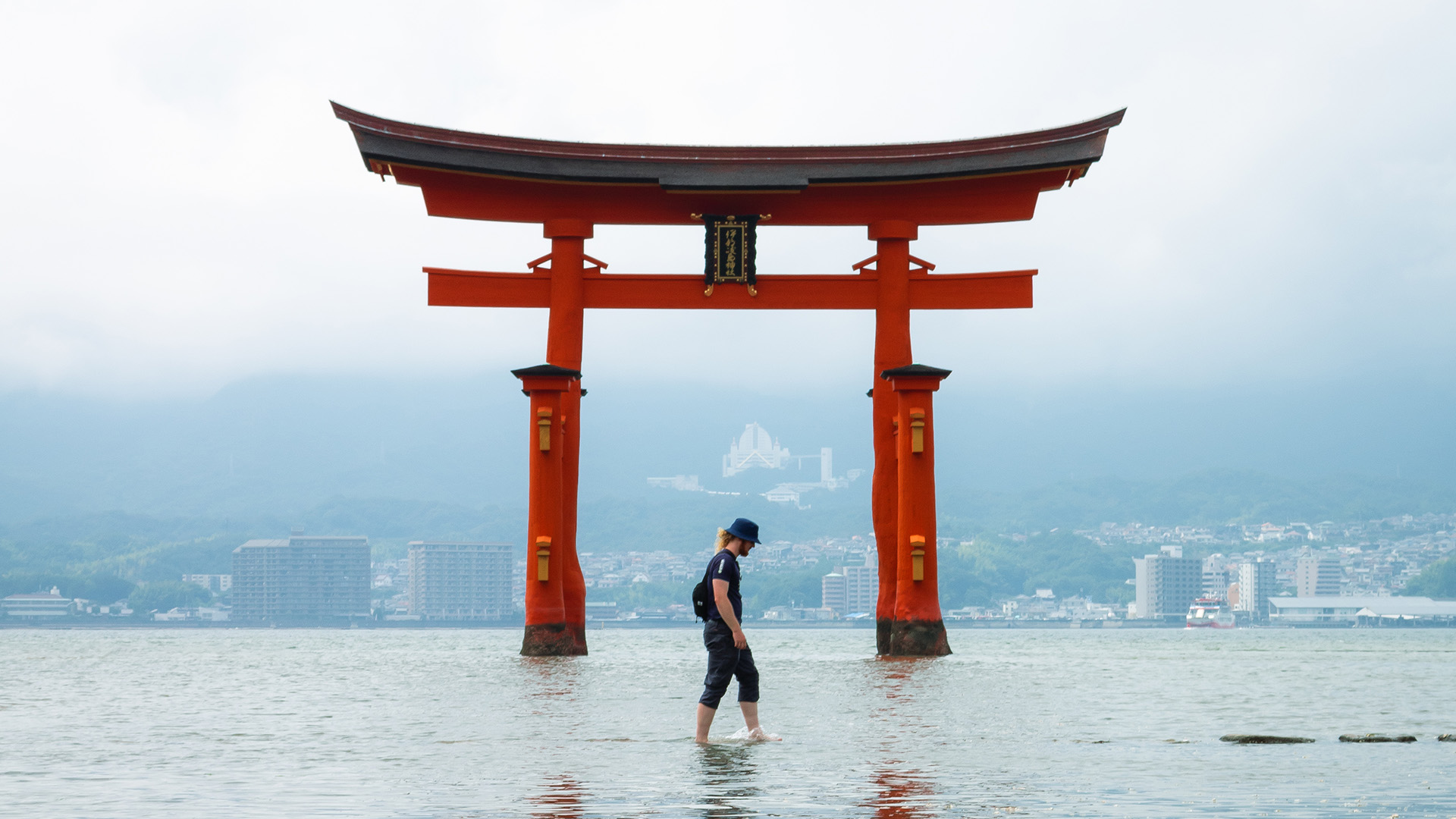 A man stands in calm water, reflecting the serene surroundings and the clear sky above.