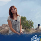 Smiling woman on rocky outcrop with misty blue mountains; Global Aggies logo