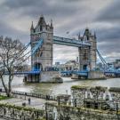 Tower Bridge in London with overcast skies and the River Thames flowing below.