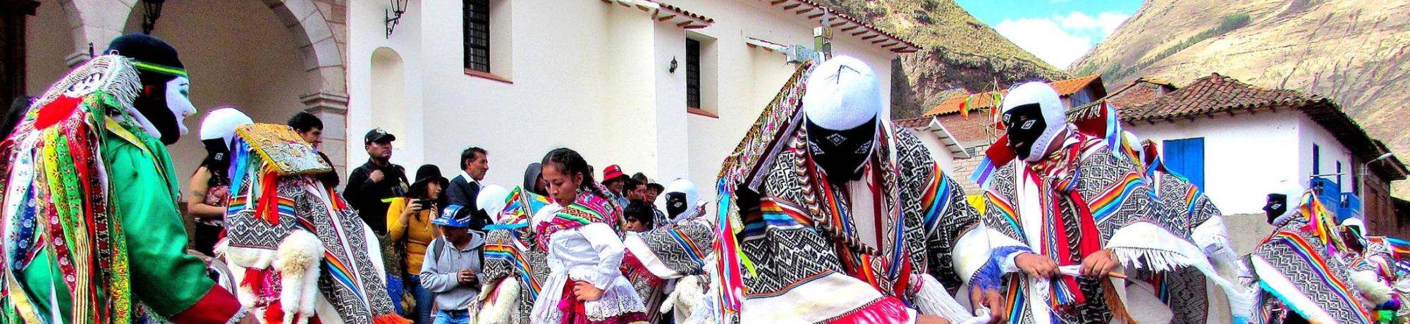Colorful dancers in traditional attire performing in a cobblestone street with mountains in the background.