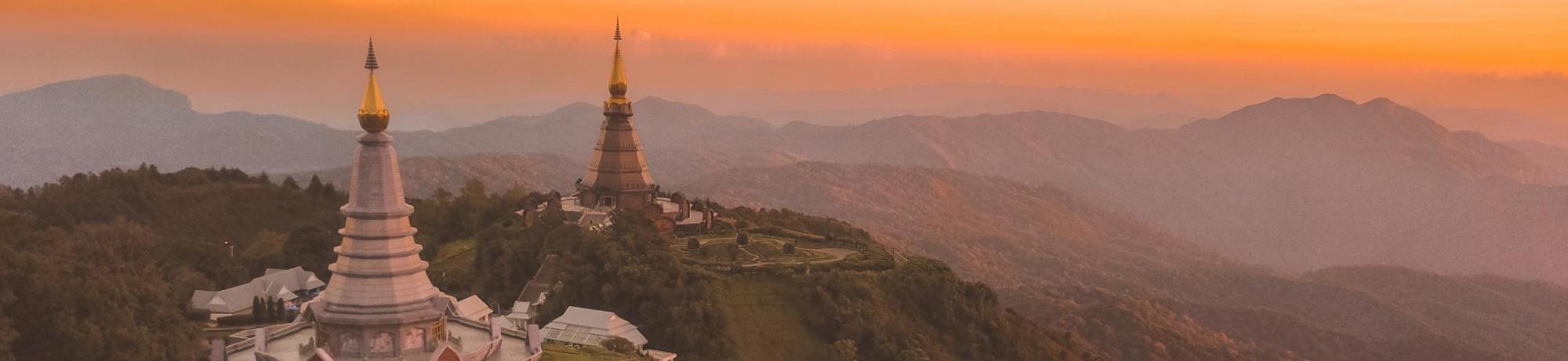 Sunset view of two pagodas on a mountain in Thailand, surrounded by misty hills.