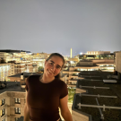 Smiling woman leaning on rooftop railing at night, city skyline with illuminated obelisk