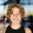 Portrait photo of smiling young person with curly blond hair, black sleeveless top