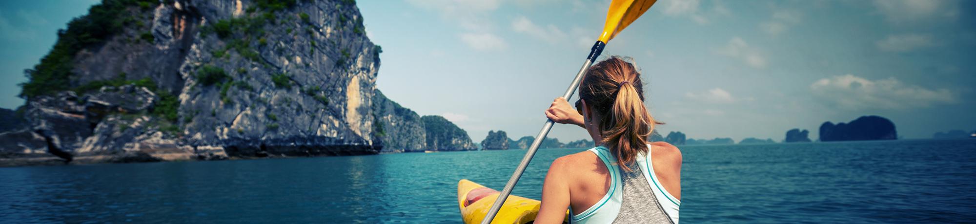 A student kayaking on calm waters with a rocky island in the distance.